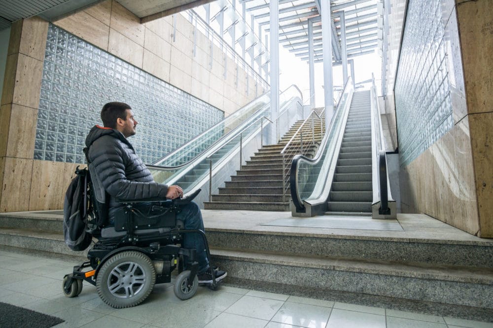 Rear View Of A Disabled Man On Wheelchair In Front Of Staircase